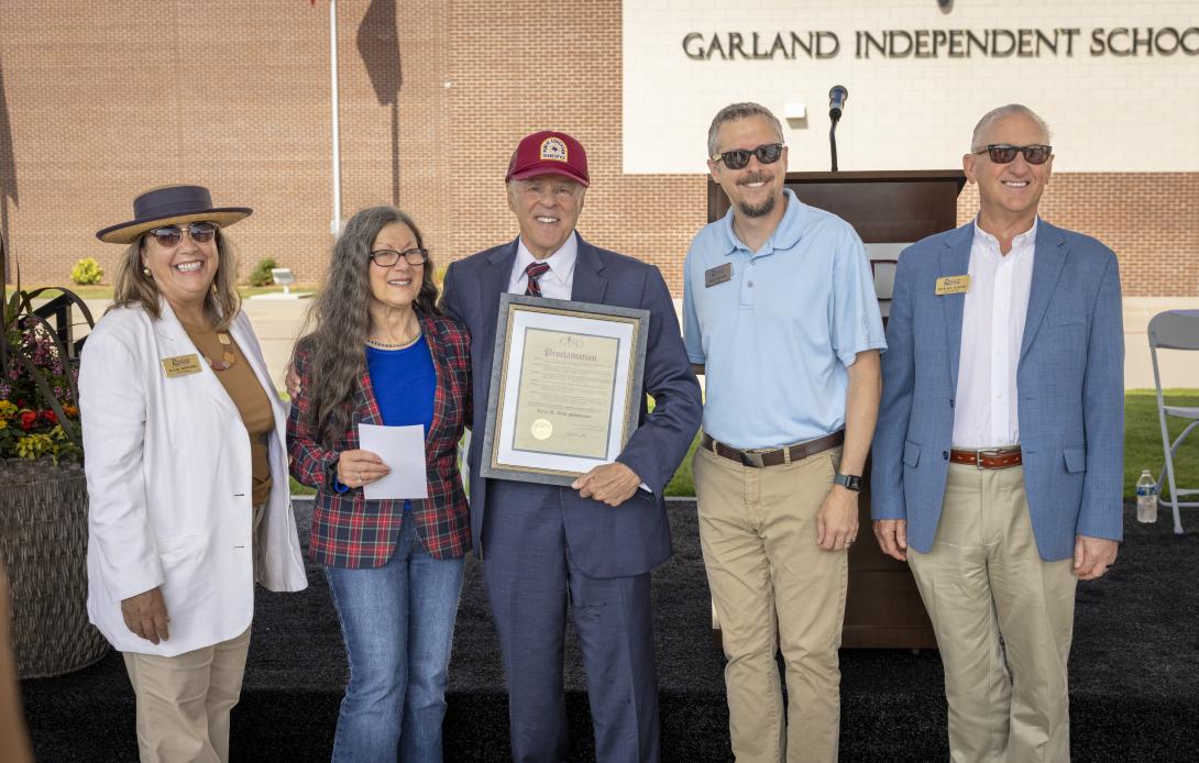 One man holds a framed document with two women standing on the left and two men on the right
