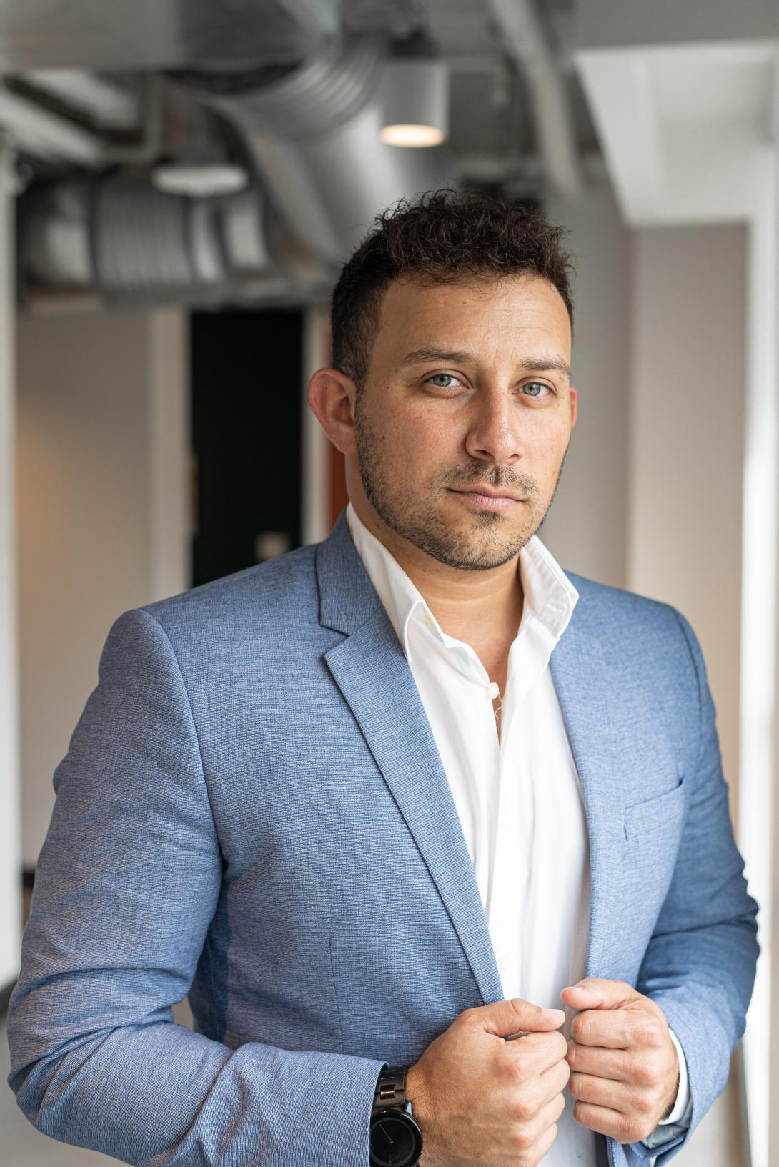 A man stands posing in a blue suit jacket looking at the camera