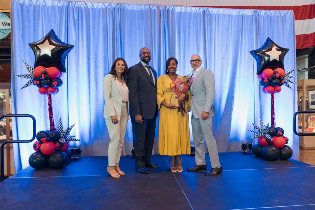 Two women and two men stand together, while one woman holds a plaque