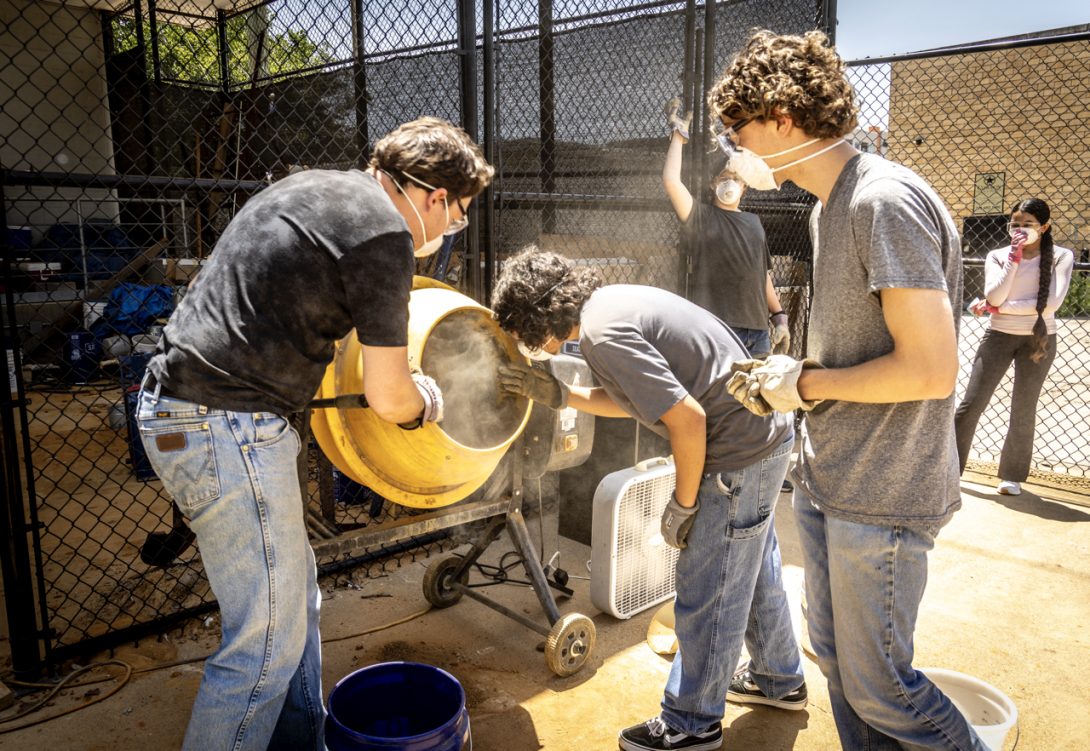 A group of male students look into a cement mixer as it turns