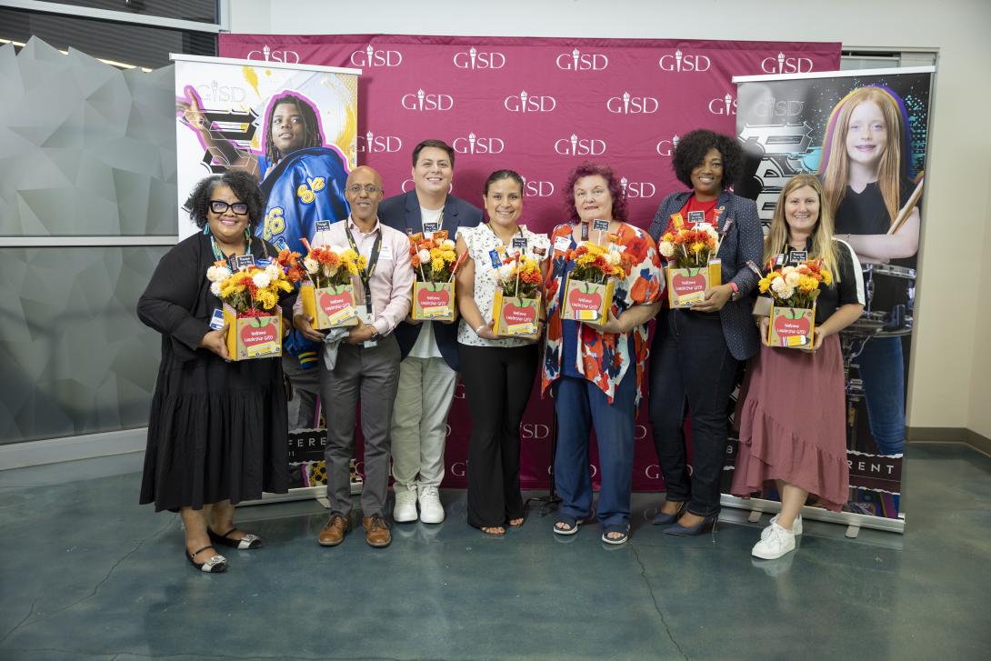 A seven-member diverse group of men and women stand holding gifts
