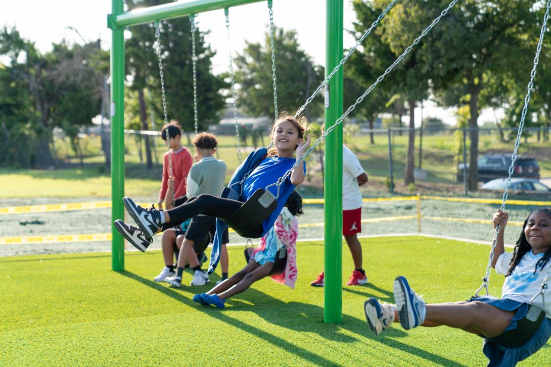 A group of young students play on a set of swings