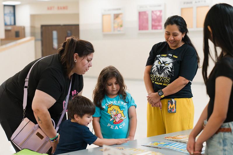 A woman smiles as a young girl picks out a book with her family