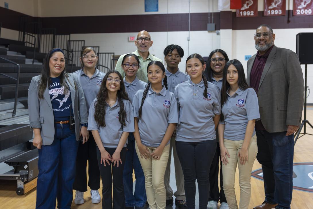 Three adults pose with a diverse group of students