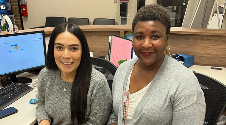 Two paraprofessionals smile for a photo at their desk.