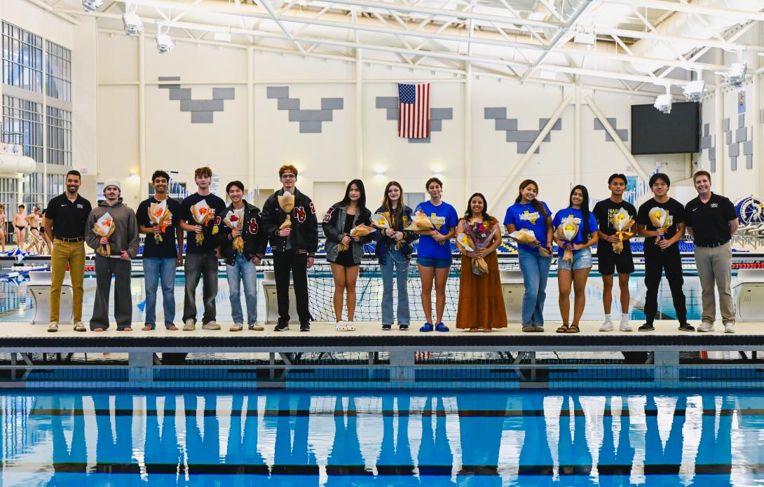 A large group of students hold flowers standing next to a pool
