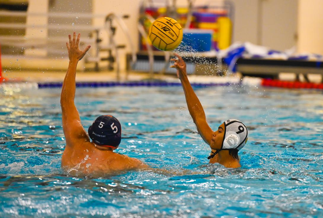 two water polo players reach for the ball