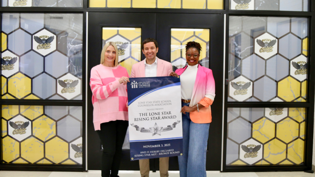 A trio of counselors stand with a banner