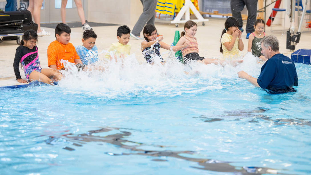A diverse group of students kick their feet in the water of a pool