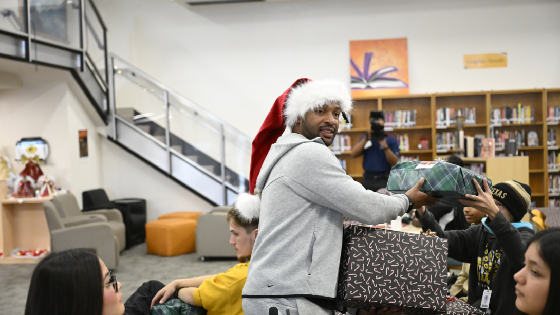 An adult man in a Santa hat distributes presents to a group of students