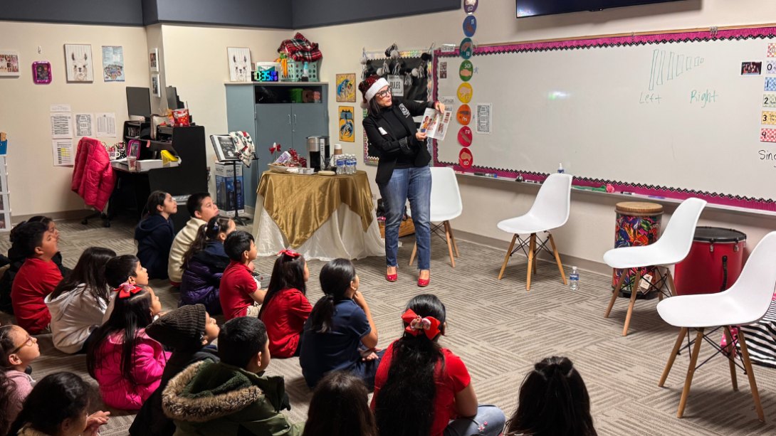 An adult woman reads to a group of students