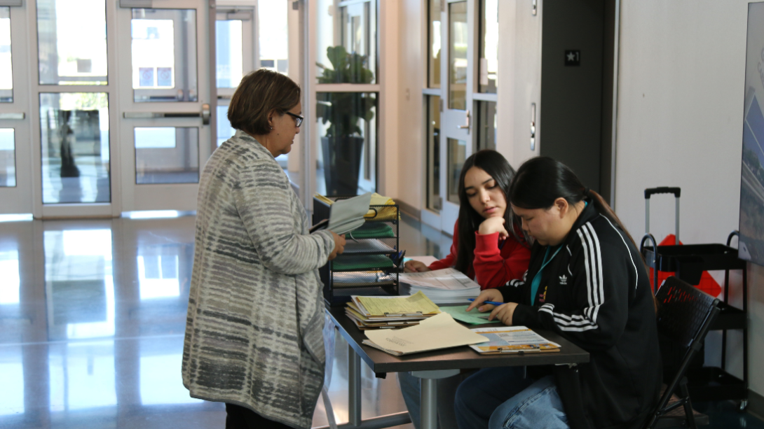 Two female students receive intake forms from a female adult