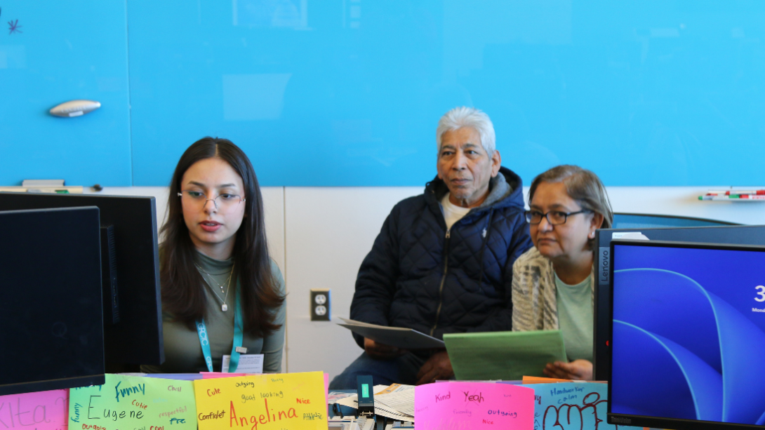 A female student works at a computer with a older couple sitting next to her