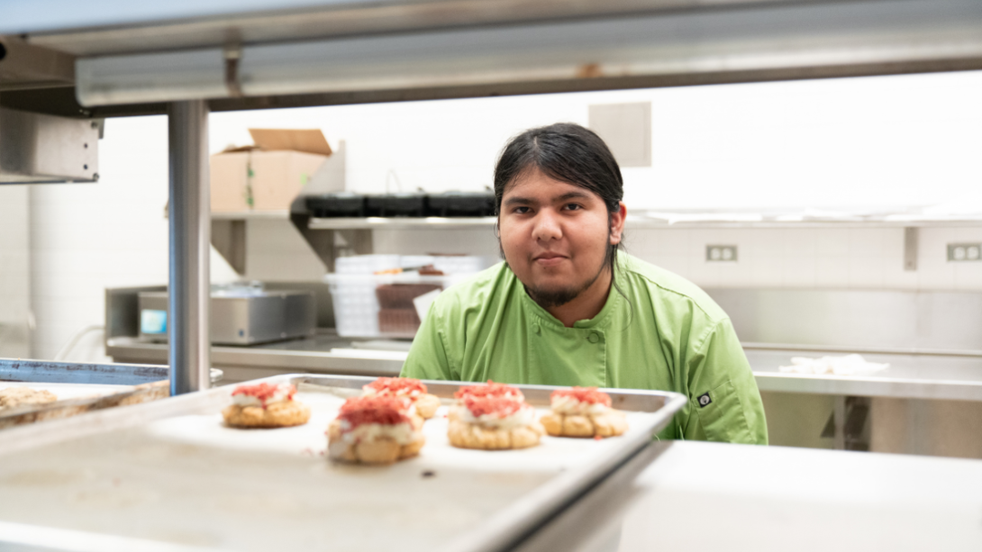 A male student stands behind a tray of baked goods