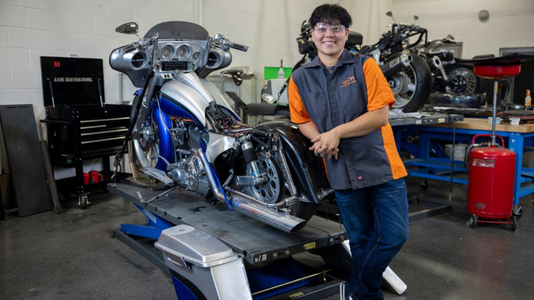 A student stands posed against a motorcycle