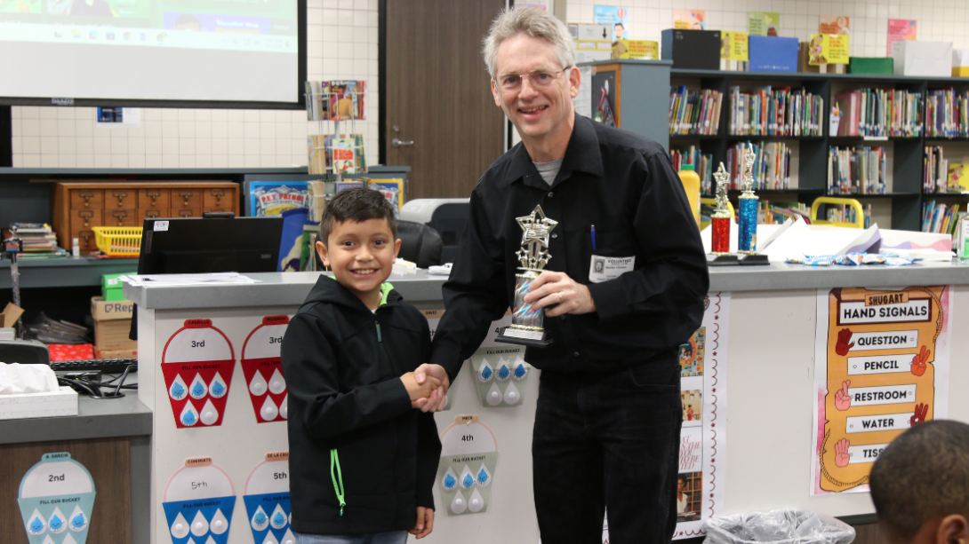 male student with trophy stands with male adult