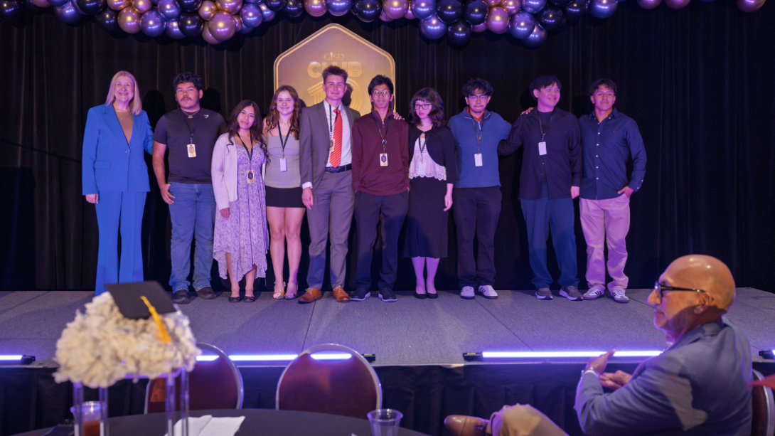 a diverse group of students stand on a stage with their principal