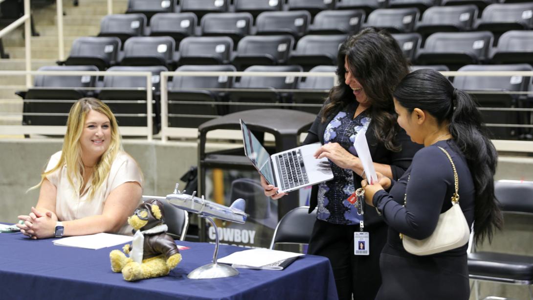 Two Armstrong Elementary staff members smile while helping a candidate find an application on a laptop.