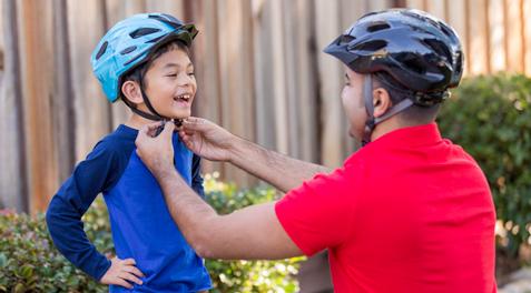 A dad helping a kid attach a bicycle helmet. 