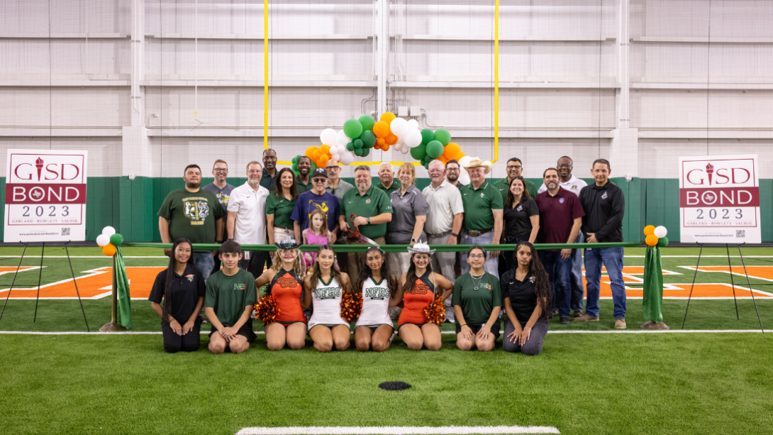 a group of students and staff kneel and stand behind a large ceremonial ribbon